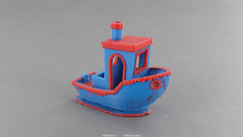 A small, 3d printed boat, with primarily a blue color for the housing, and a red trim. The print is a bit rough, with obvious layer lines and small bits of plastic sticking places.